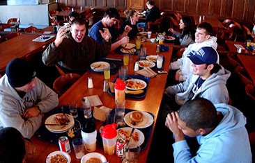 A group of seven students sit around a long table filled with food