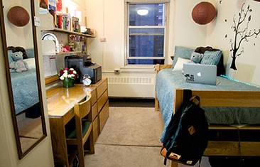 A dorm room with a desk on the left and a single bed on the right