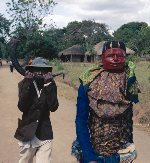 Mapiko dancer entering a village accompanied by a lipalipanda player