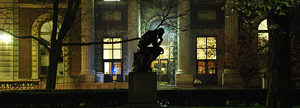 The lights of Kent Hall silhouetting the authentic iron casting of Rodin's Penseur (Thinker) in front of Philosophy Hall.