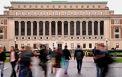 People hurry to and fro on College Walk with Butler Library in the background on a mildly overcast day