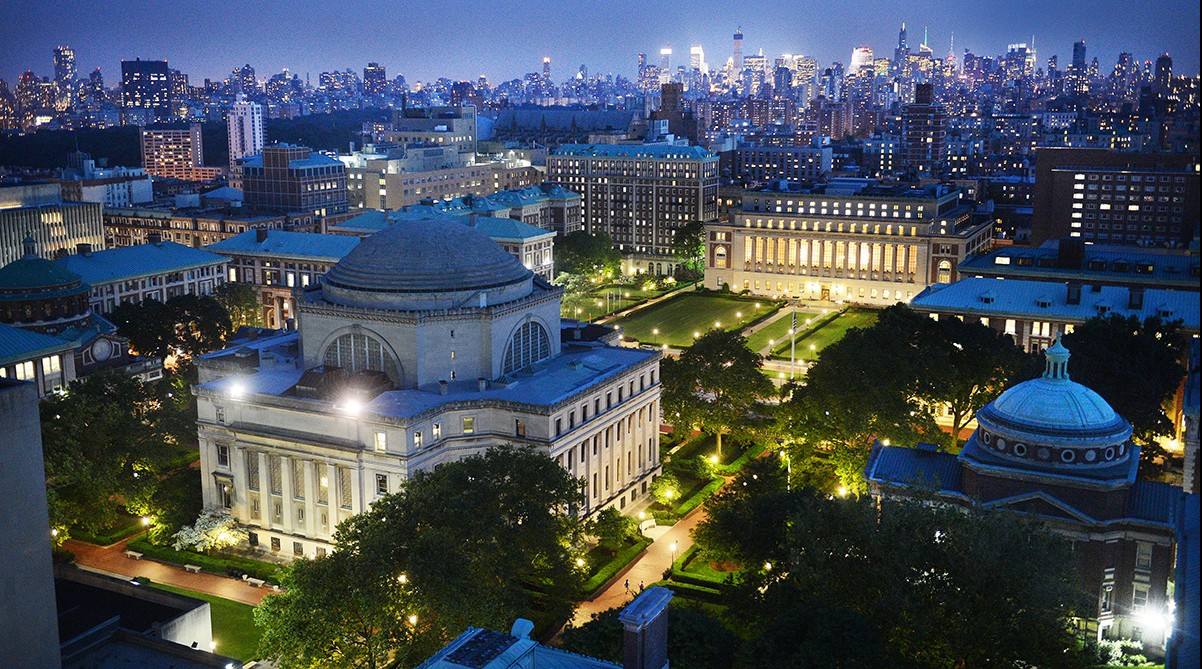 Columbia University's Morningside campus stands at dusk against the glowing New York City skyline, majestic