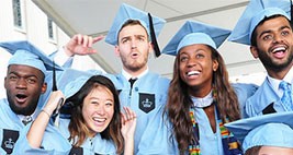 Five graduates in cap and gown celebrate facing the camera