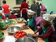 Wearing aprons and chef hats, a group of young children slice and dice an array of fresh vegetables.
