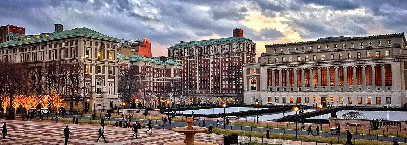 Looking south at Low Plaza and South Field, with Jon Jay Hall and Butler Library in the background, against a deep blue sky at dusk