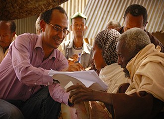 A man shares information with a woman and man, pointing to the paperwork he's holding.