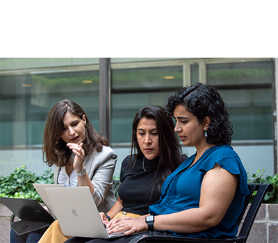 Three women talk while referencing content on a laptop.