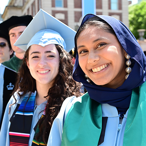 two women in mortar boards and hijab look out celebratorily