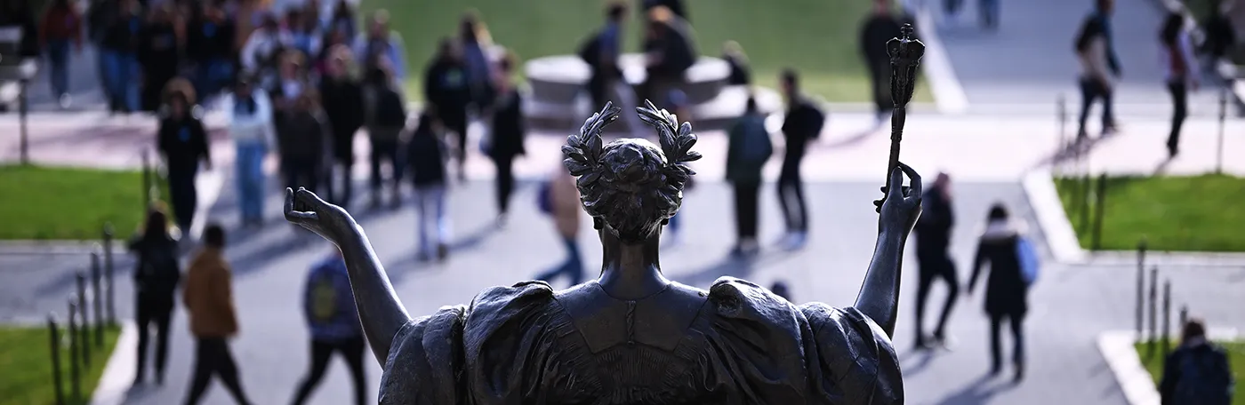 Back of the statue of Alma Mater in front of people walking on Columbia's Morningside campus.