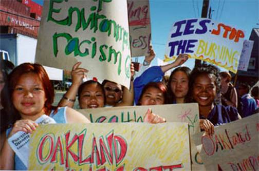 A photograph from &copy;Greenaction; http://www.greenaction.org/ Children holding up signs that say "Stop Environmental Racism" and "IES: Stop the Burning".